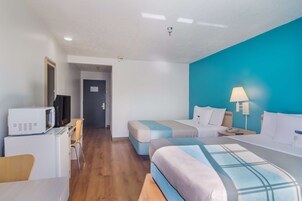 Quarto de hotel com duas camas, uma escrivaninha com micro-ondas, televisão e porta de banheiro.