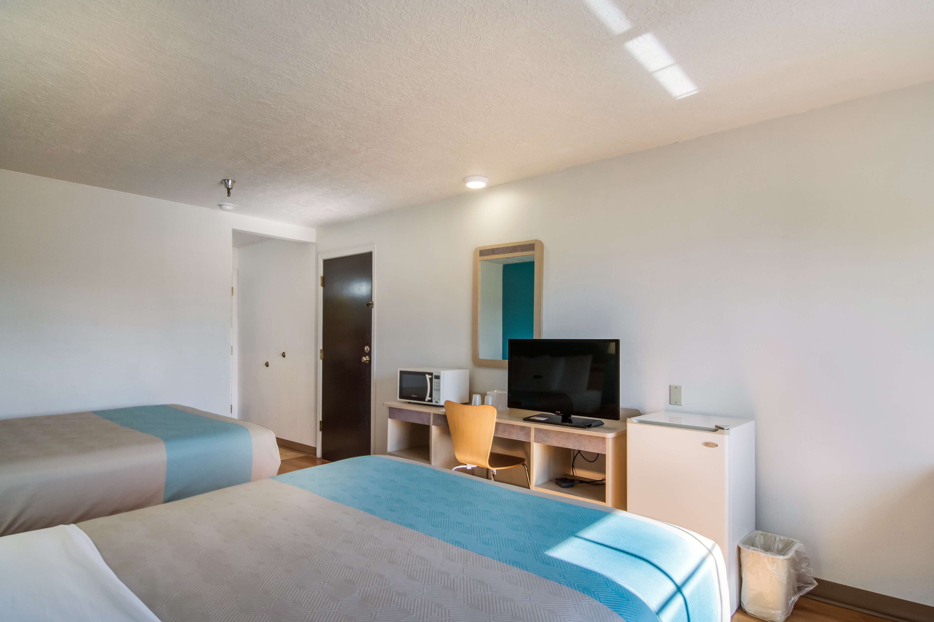 A hotel room with two beds, a desk with a computer, a television, and a microwave.
