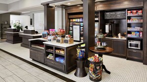 A hotel lobby with a coffee bar, snack display, and a seating area. - Hilton Garden Inn Champaign/Urbana (Champaign)