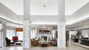 A spacious living area with a fireplace, seating, and a large window. - Hilton Garden Inn Champaign/Urbana (Champaign)