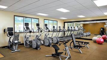 A gym with various exercise machines, a large mirror, and exercise balls.