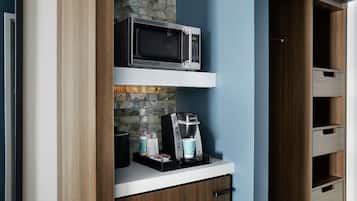 Een kitchenette met een magnetron, koffiezetapparaat en opbergladen.