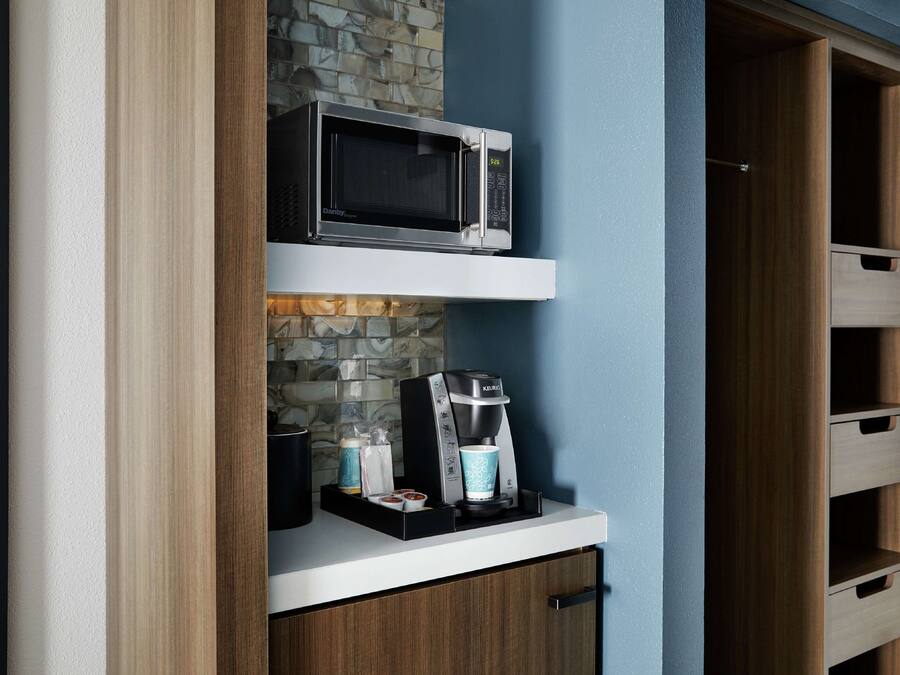 Een kitchenette met een magnetron, koffiezetapparaat en opbergladen.