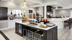 A modern breakfast bar with a variety of food items, a chalkboard menu, and bar stools. - Hilton Garden Inn Champaign/Urbana (Champaign)