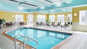 An indoor swimming pool with clear blue water, surrounded by lounge chairs and tables. - Hilton Garden Inn Champaign/Urbana (Champaign)