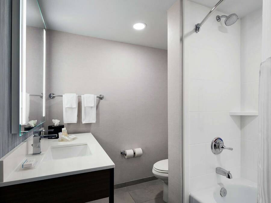 Un baño moderno con lavamanos, espejo y ducha blancos.