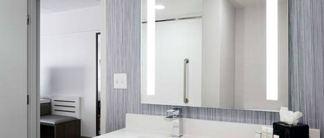 A modern bathroom with a large mirror, white sink, and a towel dispenser.