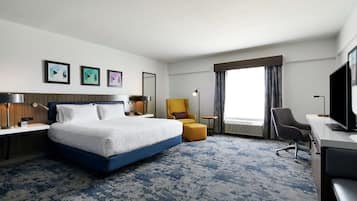 Una camera d'albergo con un letto grande, una scrivania, una sedia e un televisore. Si vedono tre quadri appesi al muro e una finestra con tende.