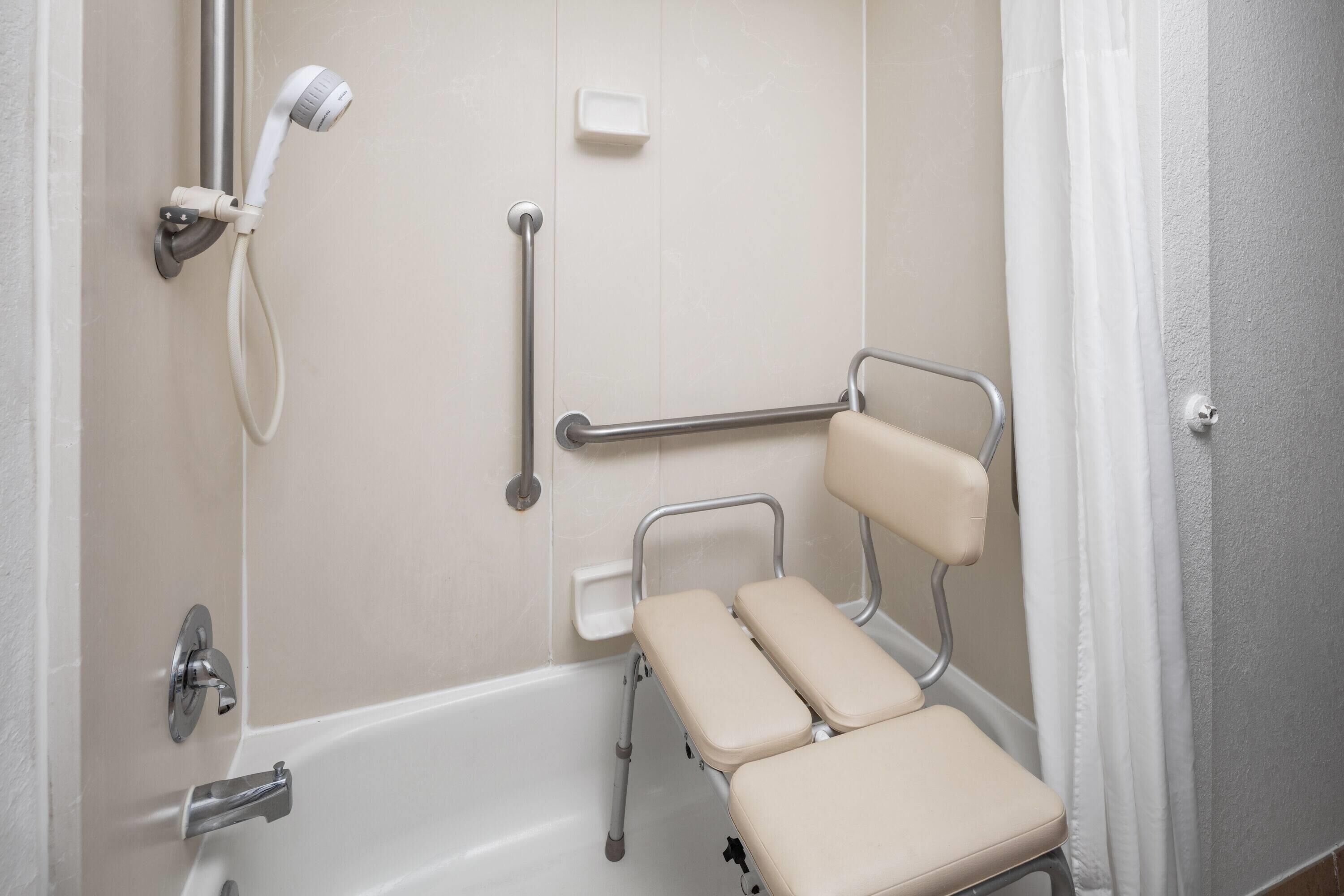 A bathroom with a bathtub, a handheld showerhead, a grab bar, and a raised toilet seat.