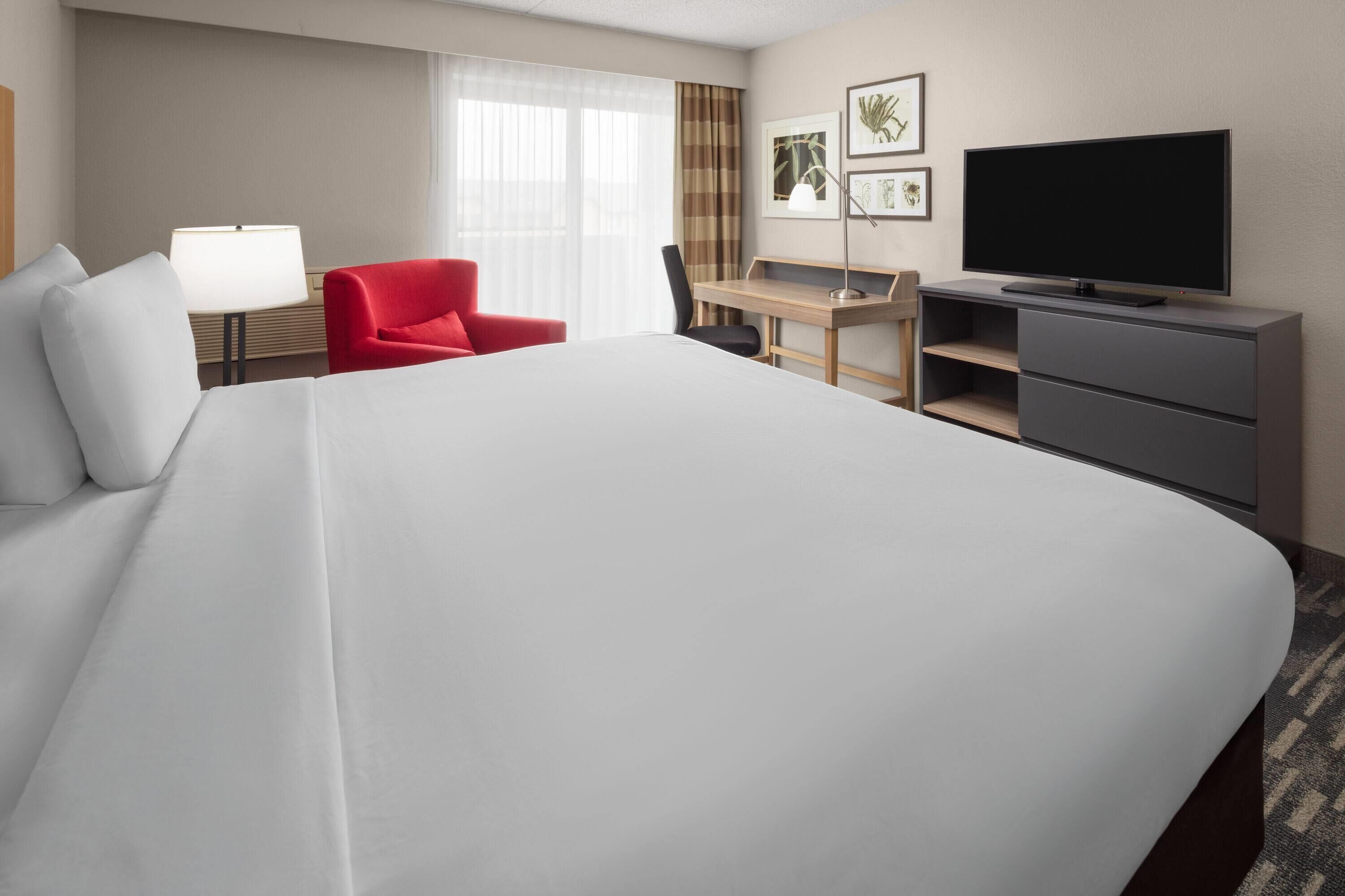 Une chambre d’hôtel avec un grand lit, un bureau avec une chaise, une télévision et un fauteuil rouge.