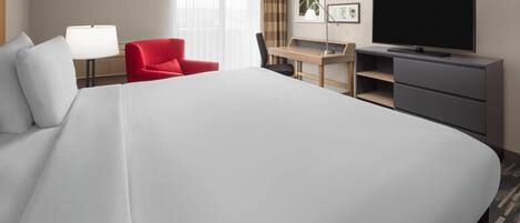 Una habitación de hotel con una cama grande, un escritorio con una silla, un televisor y un sillón rojo.