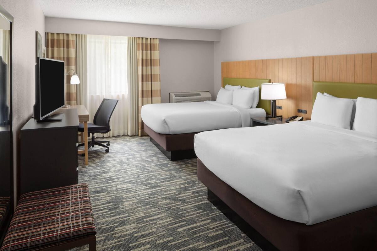 A hotel room with two beds, a desk, a television, and a chair.