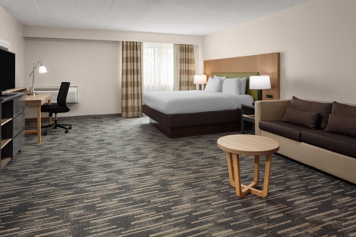 A hotel room with a bed, a sofa, a desk with a chair, a TV, and a lamp.