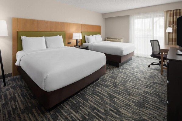A hotel room with two beds, a desk, a chair, a TV, and a window with curtains.