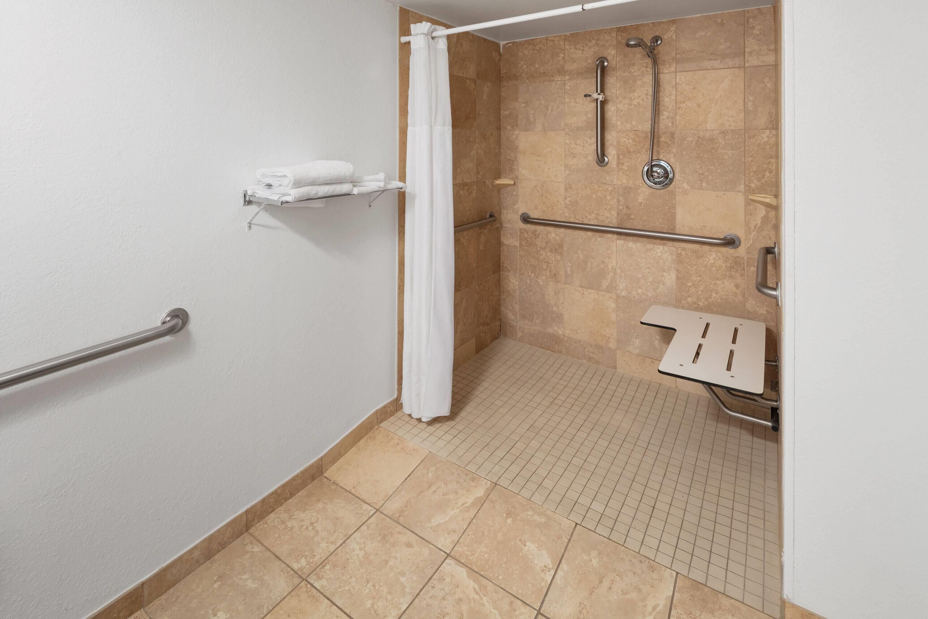 A handicap-accessible bathroom with a shower, grab bars, and a white towel rack.