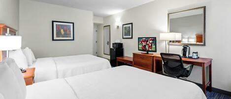 A hotel room with two beds, a desk, a chair, a television, a coffee maker, and framed artwork on the walls.
