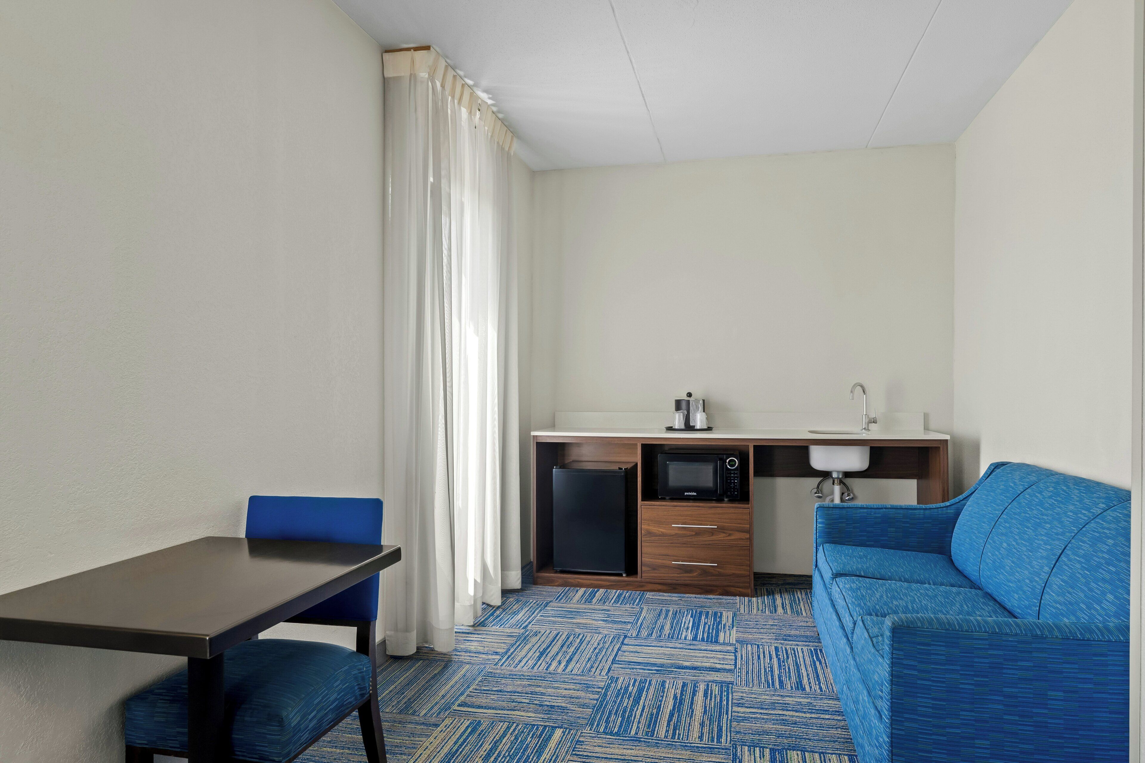 Quarto compacto com mesa de jantar, cadeira azul, cozinha compacta e sofá azul.