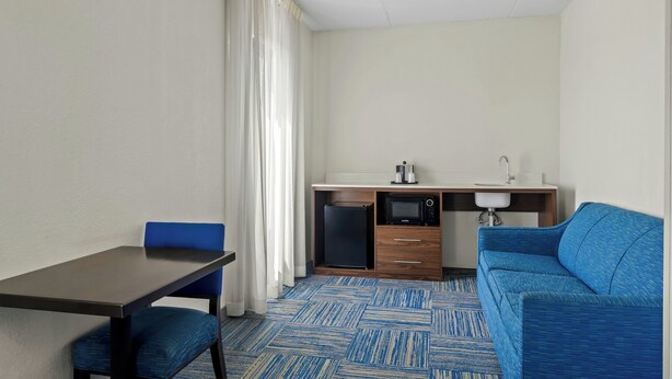A compact room with a dining table, blue chair, kitchenette, and a blue sofa. - Allentown Park Hotel by The Red Collection (Allentown)