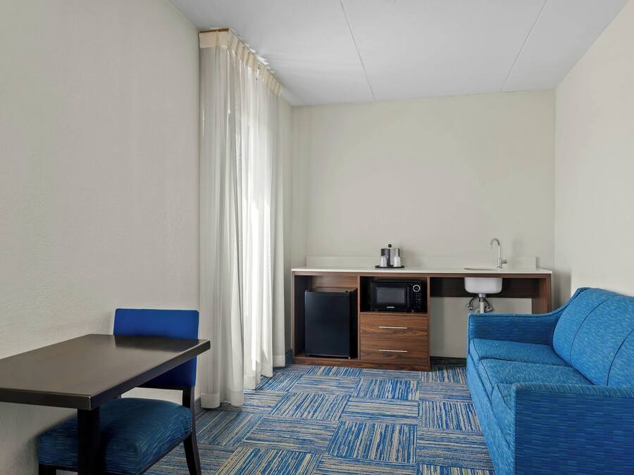 Habitación compacta con mesa de comedor, una silla azul, kitchenette y un sofá azul.