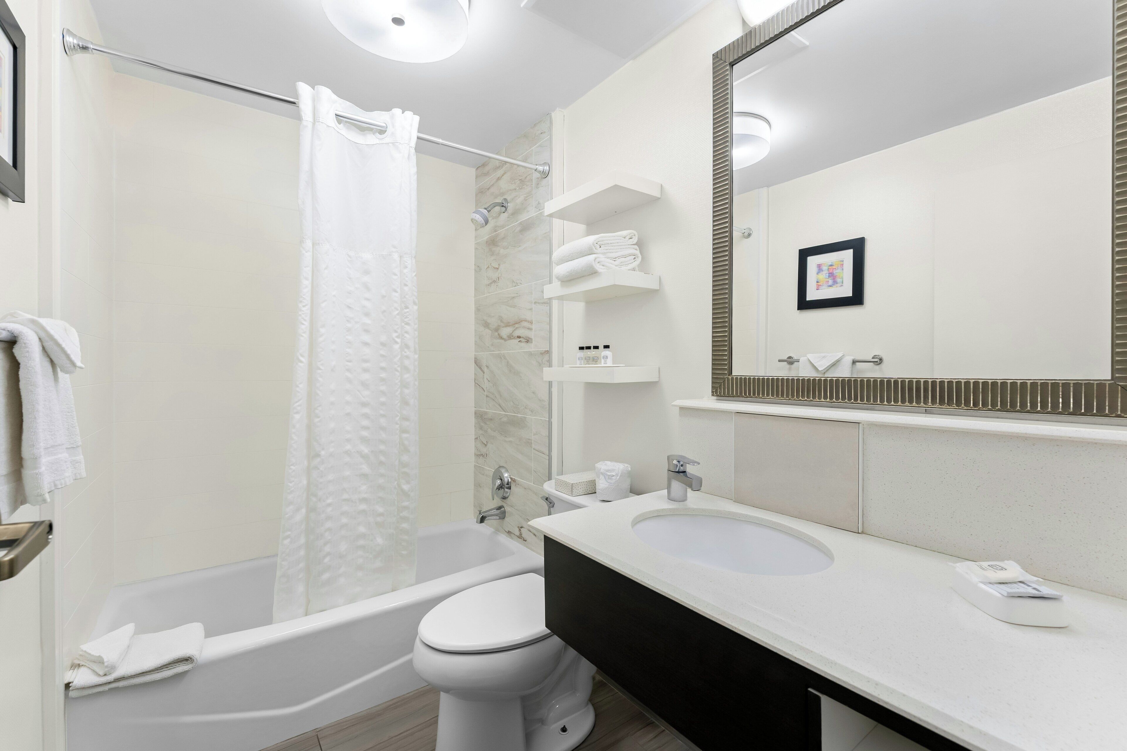 A modern bathroom with a bathtub, toilet, and sink, featuring a large mirror and towel racks.