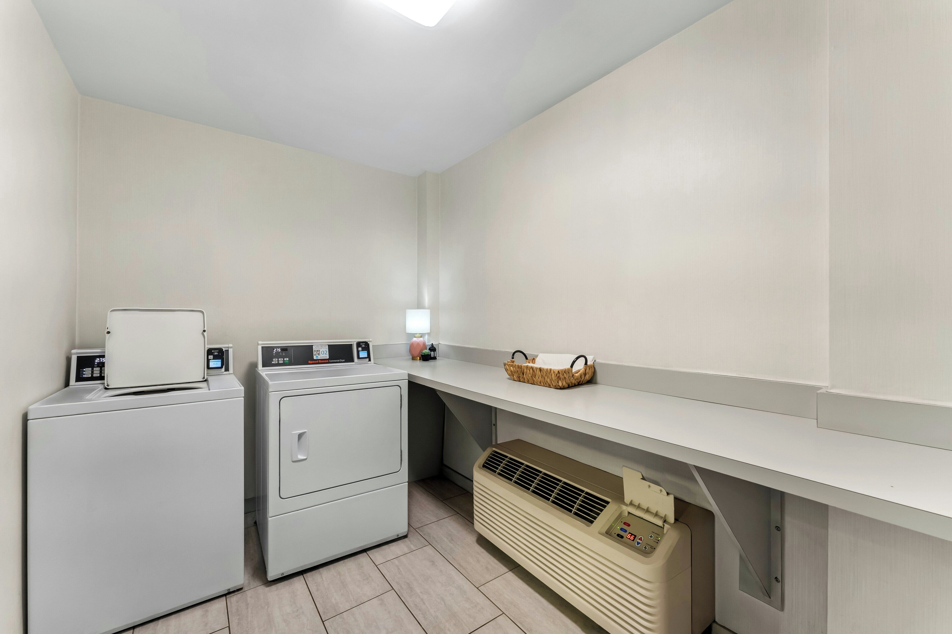 A laundry room with two washing machines, a dryer, a heater, and a basket on a shelf.