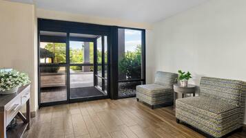 A modern room with a sliding glass door leading to an outdoor area, a patterned armchair, a small round table with a plant, and a console table with drawers.