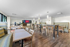 Un hall d’hôtel moderne avec un espace repas, un bar et une cuisine en arrière-plan.