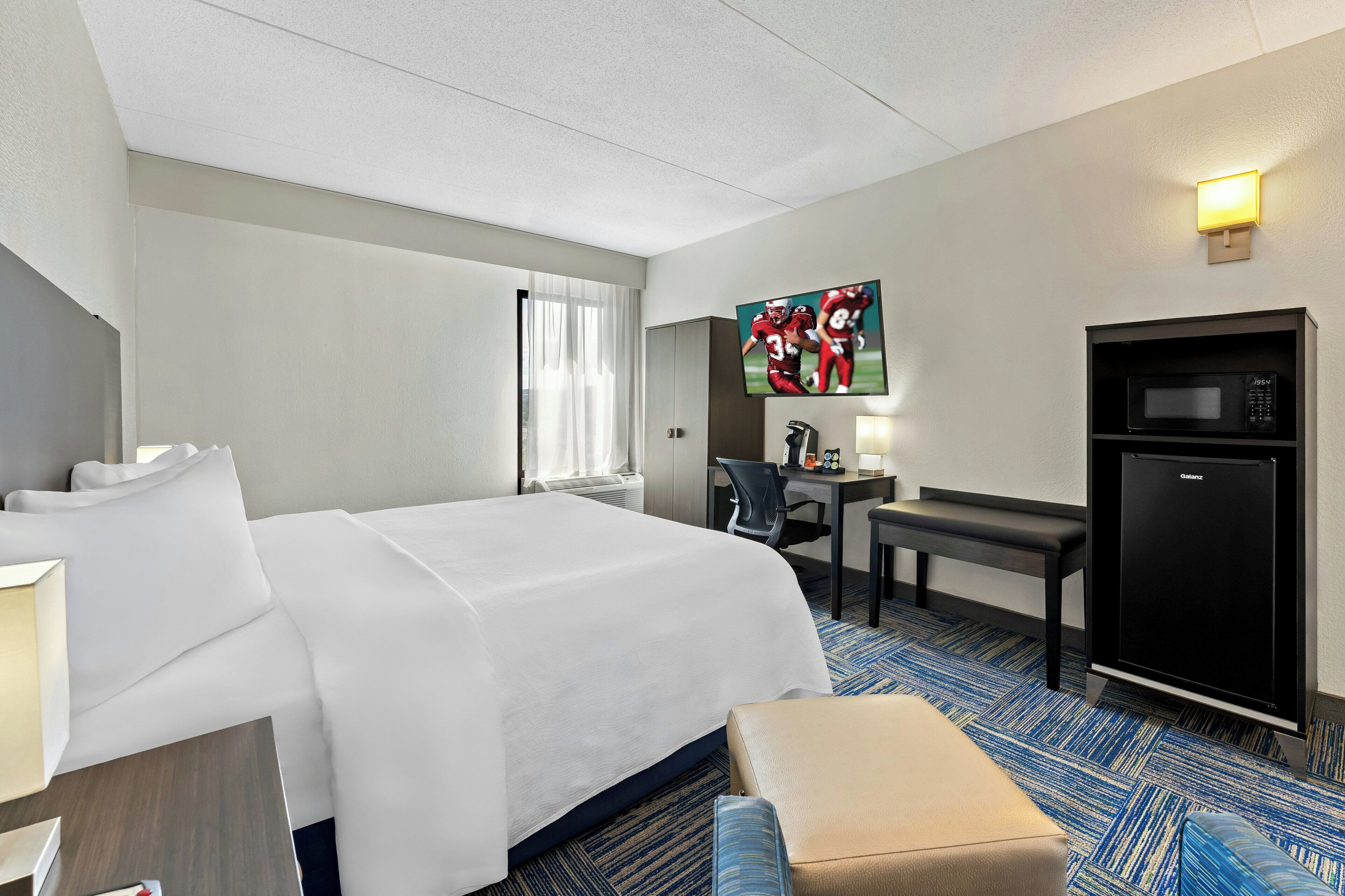 Habitación de hotel con una cama grande, un escritorio con silla, un microondas y un televisor en la pared.
