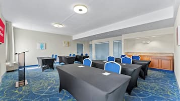 Un salón de conferencias con mesas, sillas, un atril y piso alfombrado.