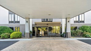 A modern building entrance with a covered patio, glass doors, and a bench. - Allentown Park Hotel by The Red Collection (Allentown)