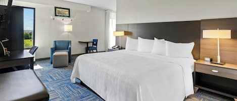 A hotel room with a large bed, a desk, a chair, a TV, and a window with a view.