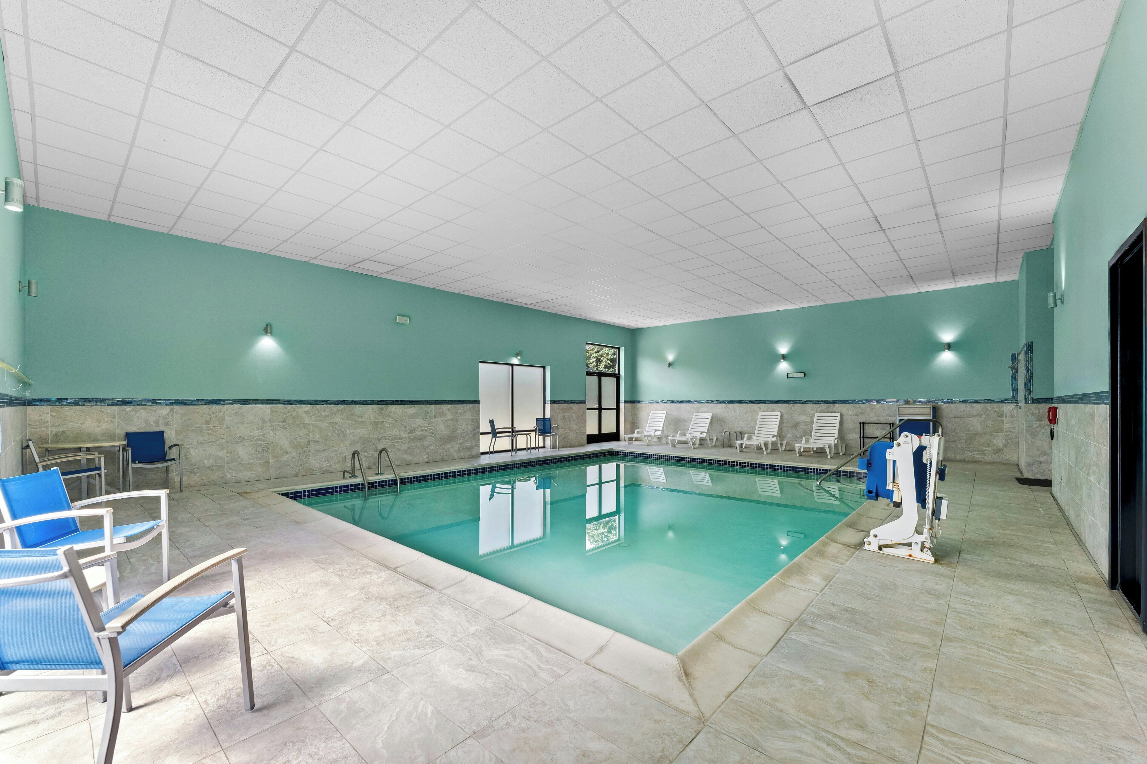 Una piscina interior con agua cristalina, rodeada de sillones de descanso y suelo de baldosas.