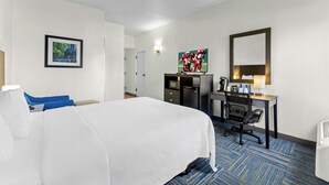 Una habitación de hotel con cama, escritorio, silla, televisor y espejo.