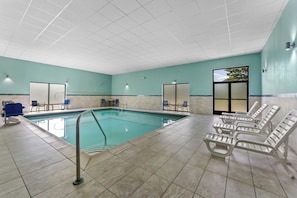 Une piscine intérieure avec un sol carrelé, des chaises longues et une vue sur les arbres à travers une fenêtre.