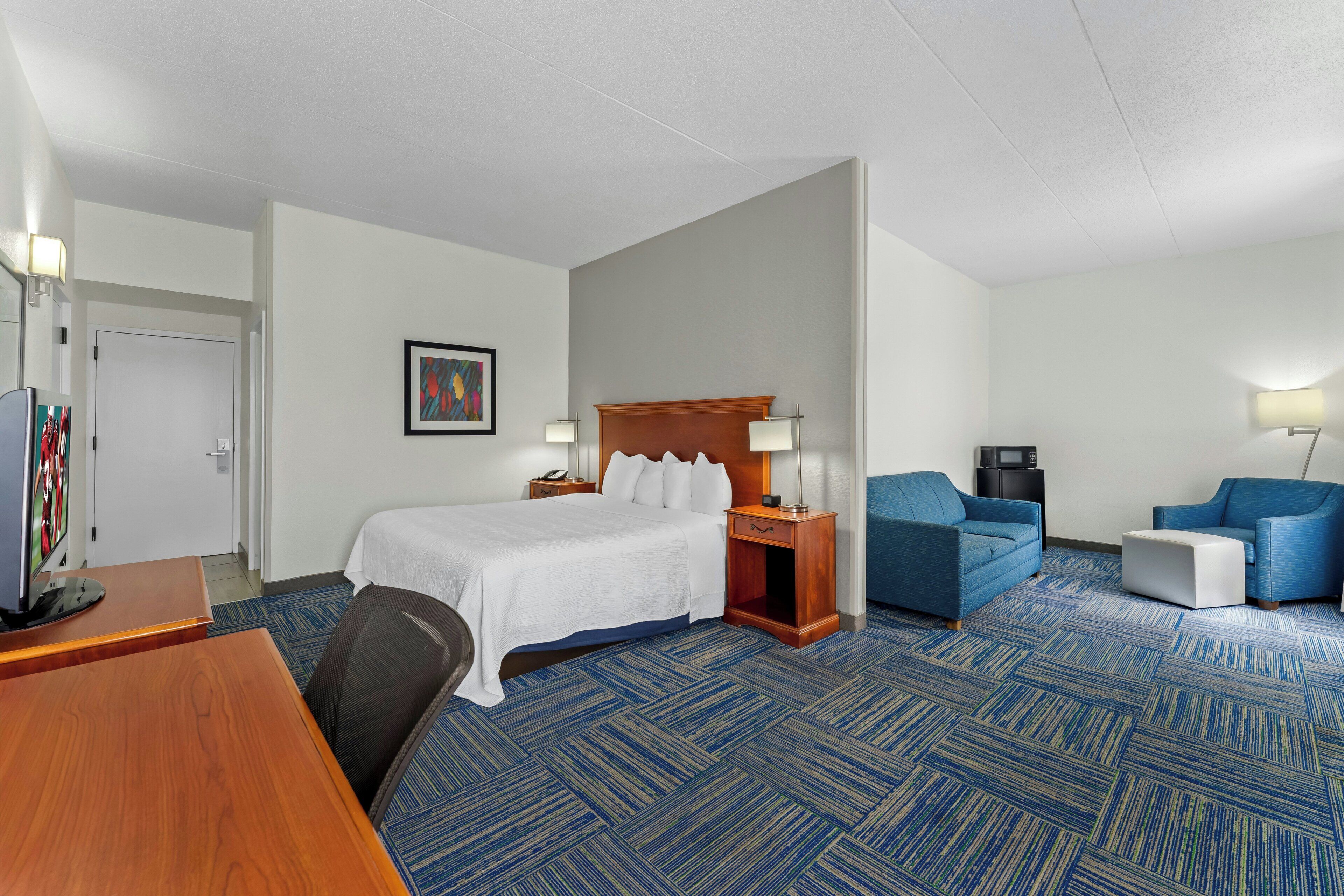A hotel room with a bed, two armchairs, a desk, and a TV.