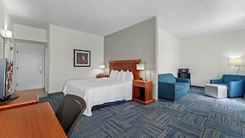 A hotel room with a bed, two armchairs, a desk, and a TV.
