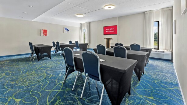Un salón de conferencias con mesas, sillas, una pantalla de proyector y un ventanal grande.
