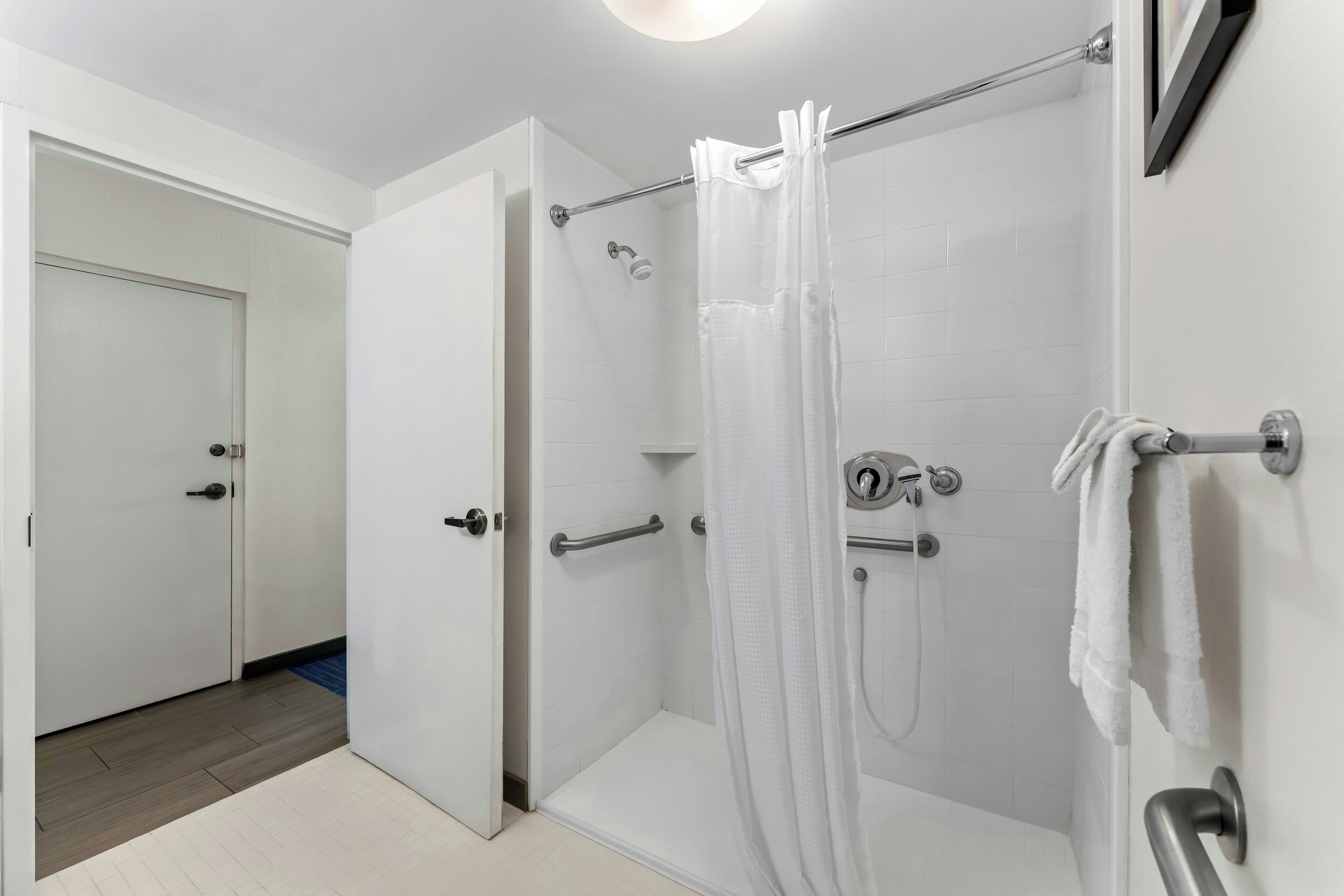 Un baño moderno con cabina de ducha de vidrio, un perchero y una puerta visible que conduce a otra habitación.