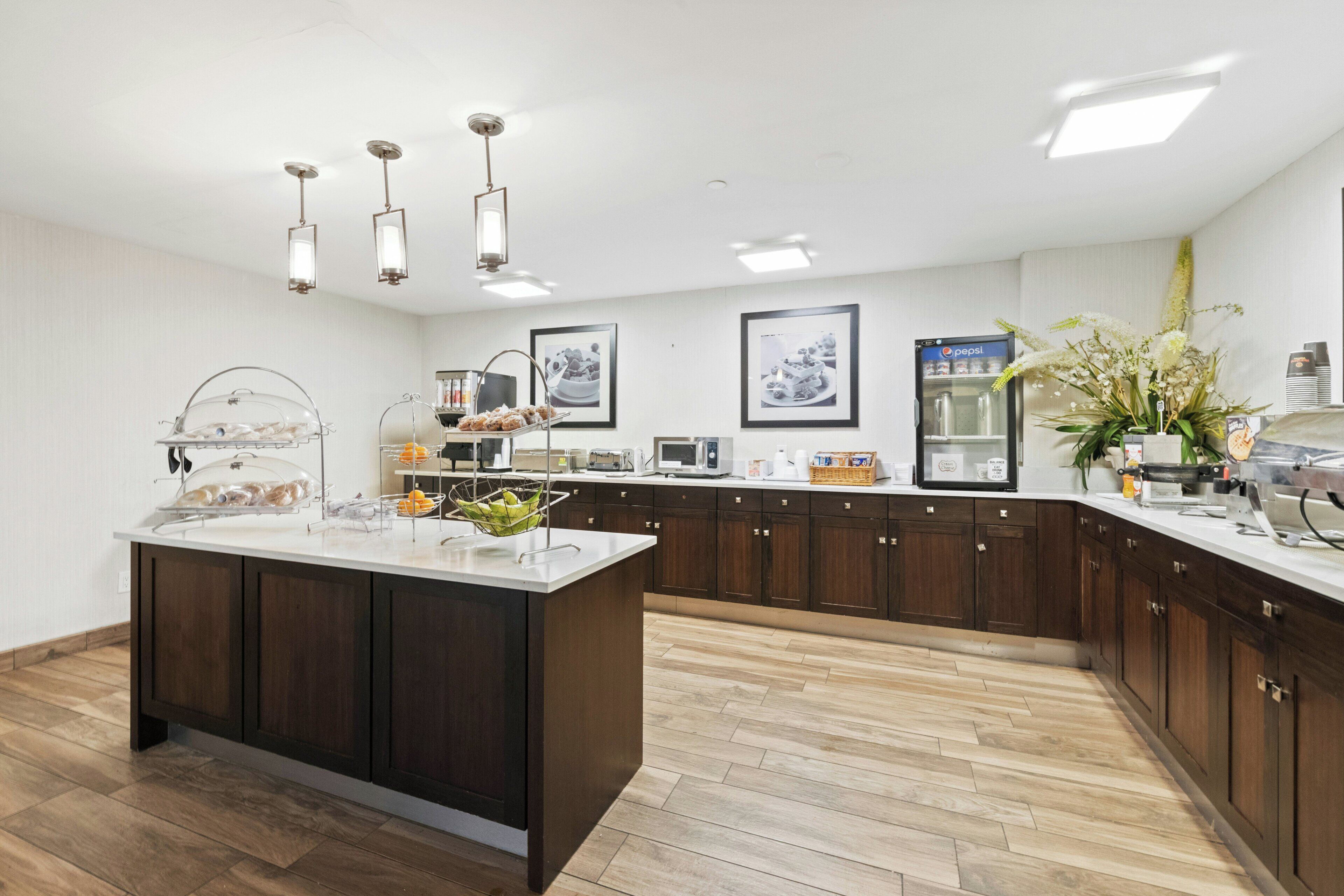 A modern kitchen with a central island, overhead lighting, and a refrigerator with a Pepsi logo.