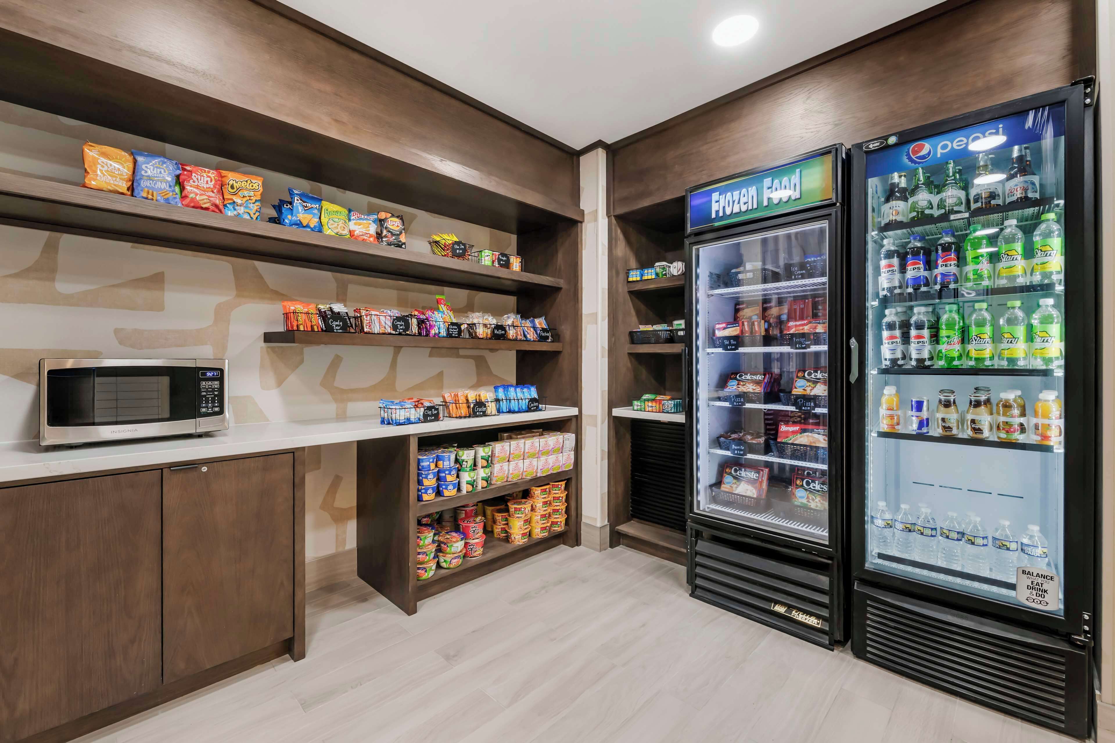 Bereich für Snacks und Getränke mit Mikrowellen, Regalen voller Snacks und zwei Kühlschränken, auf denen „Tiefkühlkost“ und „Balance“ stehen.