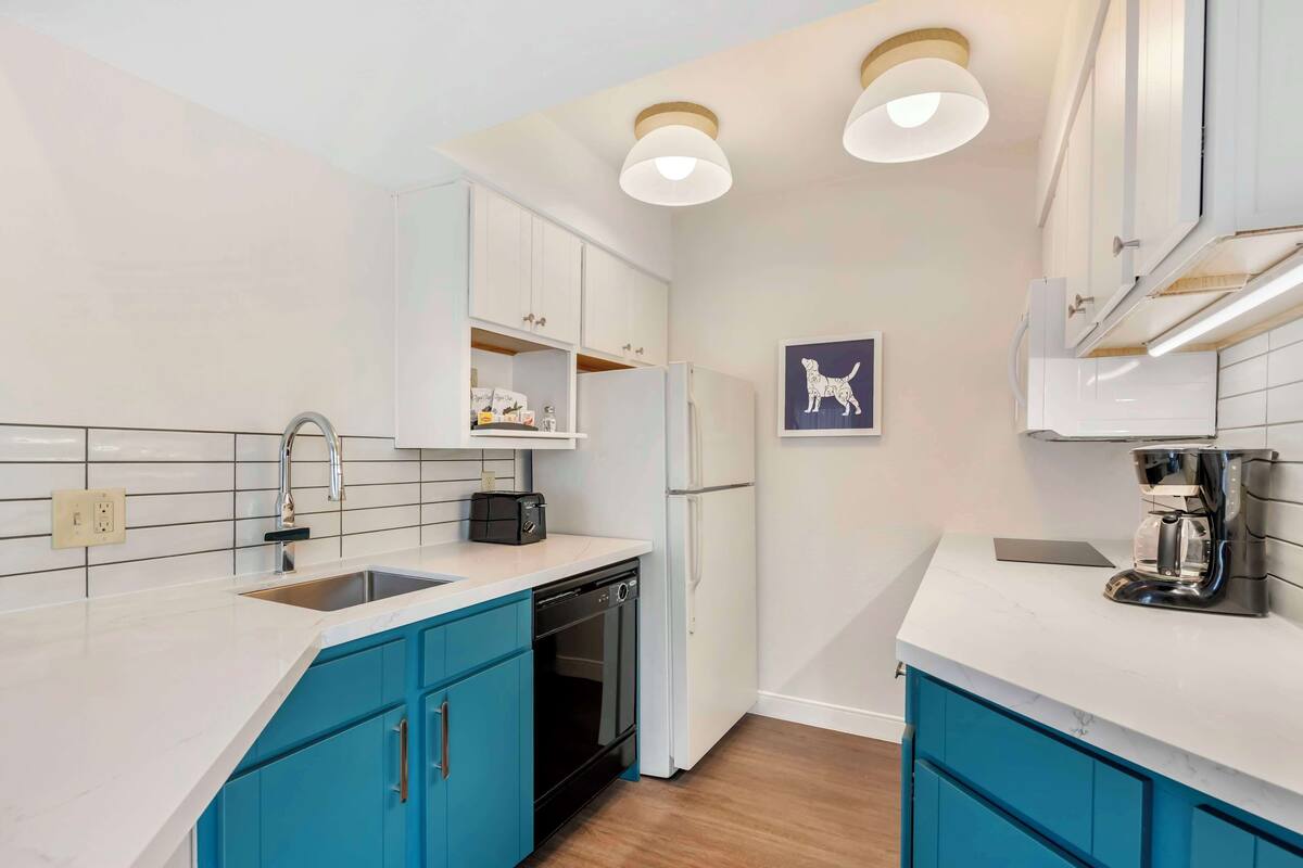 A modern kitchen with white cabinets, blue accents, a dishwasher, and a coffee maker.