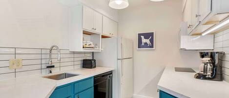 A modern kitchen with white cabinets, blue accents, a dishwasher, and a coffee maker.
