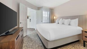 A hotel room with a large bed, a TV on a wooden console, a bedside table, and a door leading to another room.