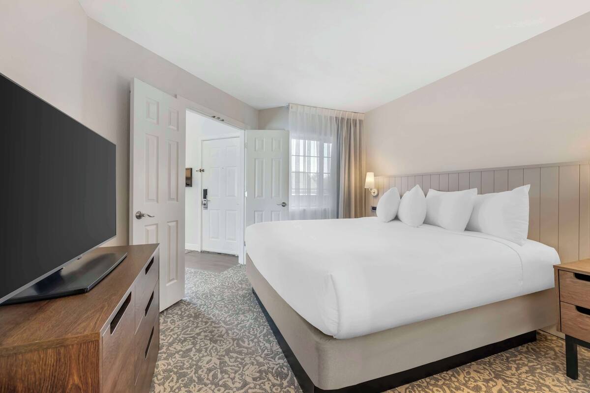 A hotel room with a large bed, a TV on a wooden console, a bedside table, and a door leading to another room.