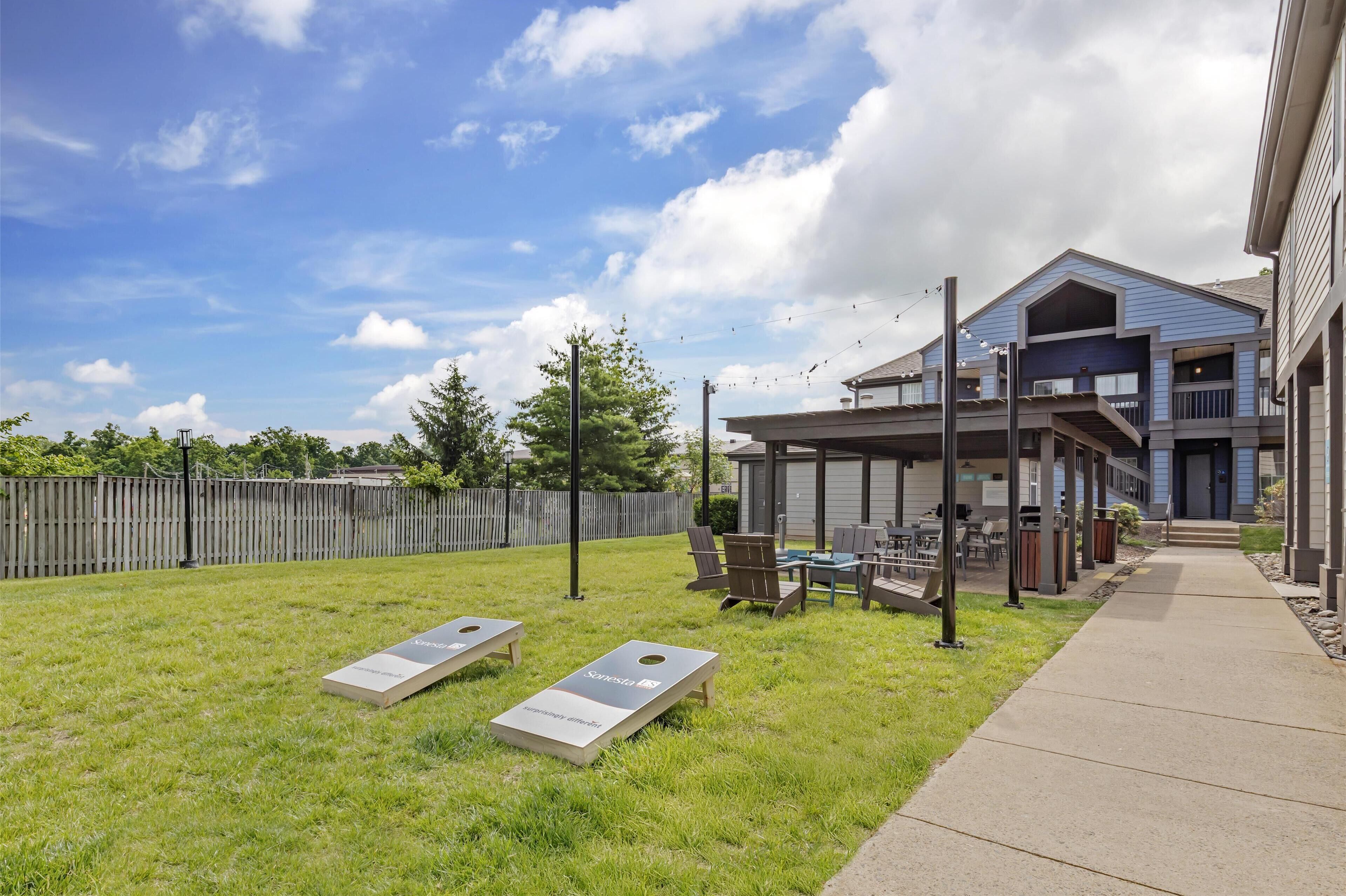 A backyard with a lawn, two bean bags, a barbecue grill, and a covered patio area with outdoor furniture.