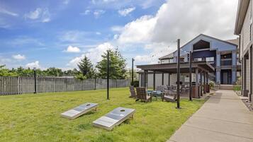 A backyard with a lawn, two bean bags, a barbecue grill, and a covered patio area with outdoor furniture.