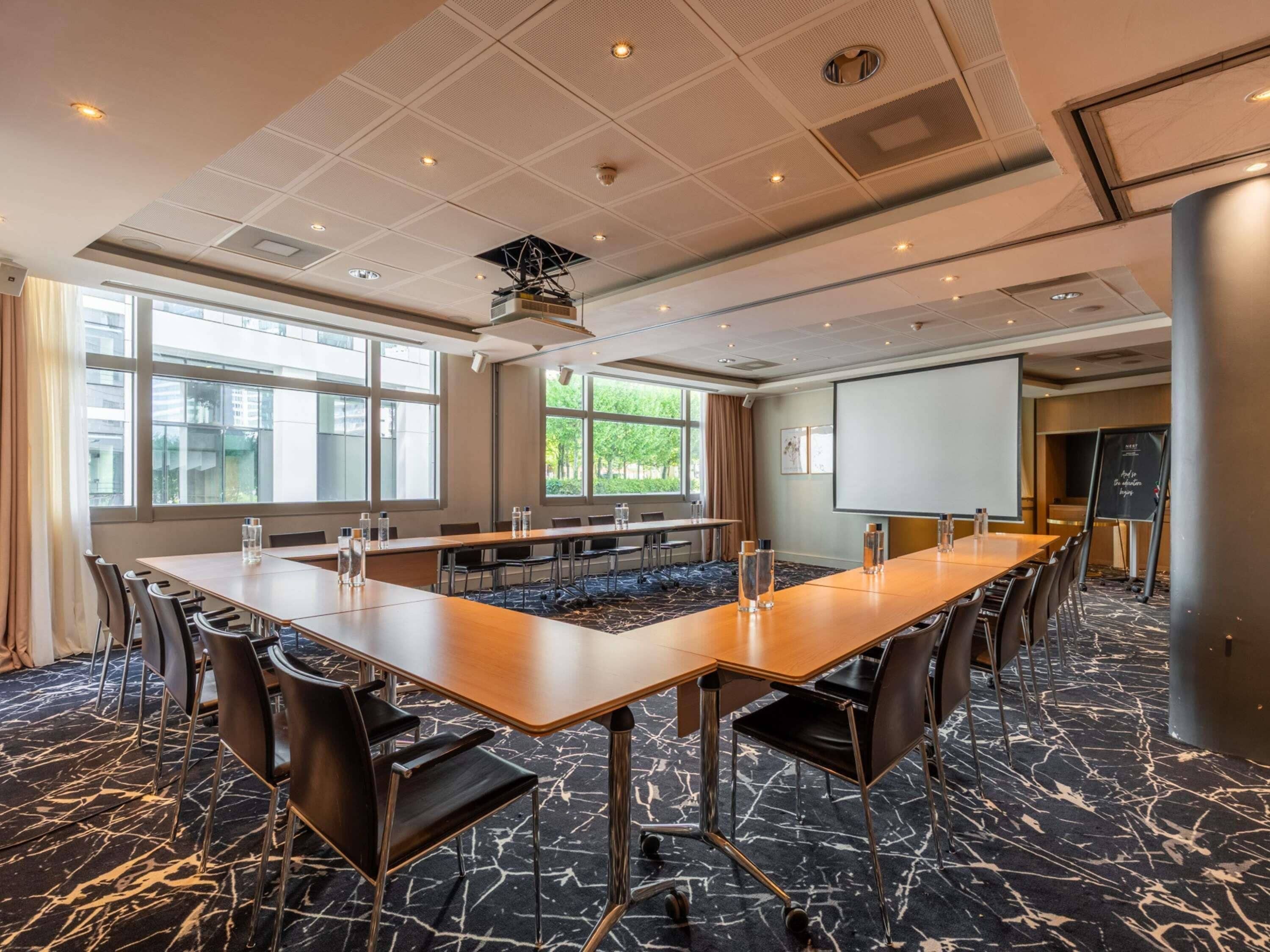 A conference room with a long table, chairs, a projector screen, and a large window.