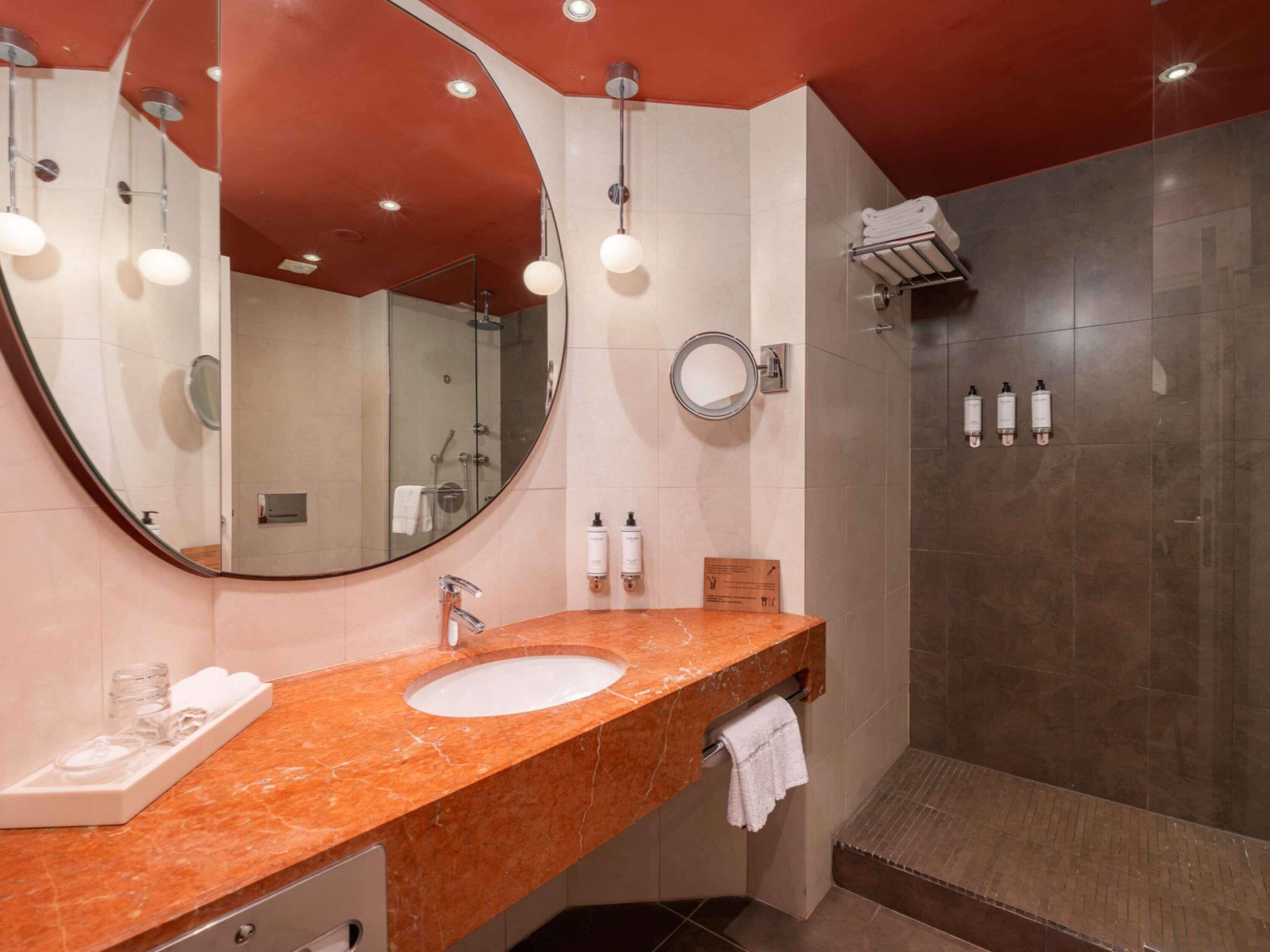 Ein modernes Badezimmer mit Marmorwaschtisch, großem Spiegel, Dusche und Handtuchhalter.