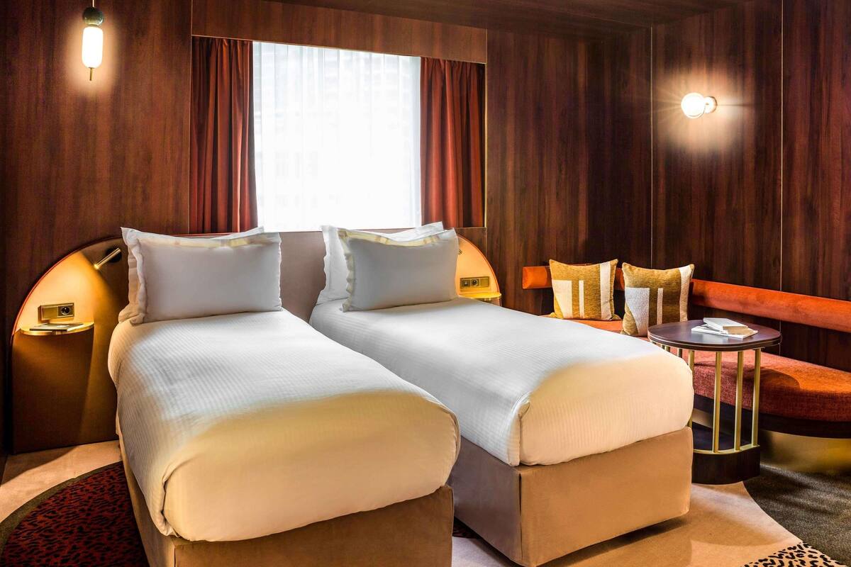A hotel room with two beds, a round table, and a large window.