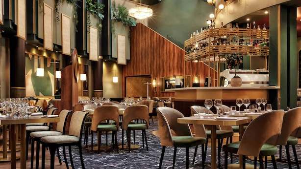 Un restaurant moderne doté d’un plafond haut, éclairé par la lumière naturelle filtrant à travers des puits de lumière, et comprenant un espace bar avec une étagère en bois.